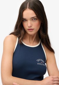 Granatowy, żeberkowany top bez rękawów z kremowym wykończeniem, z nadrukowanym logo "Superdry Athletics" z przodu. Dopasowany krój.