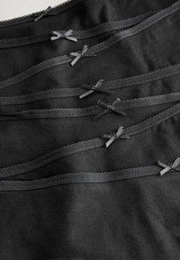 Tessuto nero con bordino in pizzo ondulato e piccoli fiocchi in satin neri, disposti in linee orizzontali, creando un effetto di texture a strati.