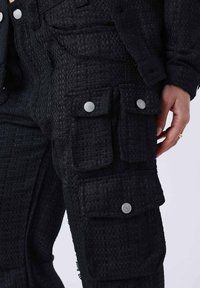 Pantaloni cargo neri a trama con multiple tasche a pattina con bottone. Presentano dettagli in metallo argentato e un motivo intrecciato per un tocco in più.