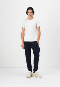 Hvid kortærmet T-shirt, marineblå joggerbukser med snøre og beige sneakers. Enkel, afslappet påklædning med minimalistisk design.