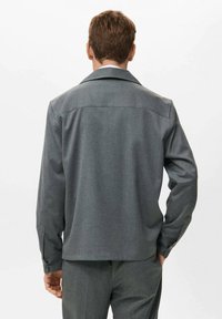 Chaqueta gris de tejido trenzado con cuello americano, mangas largas y dobladillo recto. La parte trasera incluye un yugo y un diseño ligeramente ajustado.