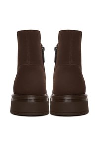 Paire de bottines en daim marron foncé avec fermetures éclair latérales et semelles épaisses en caoutchouc, vues de dos sur fond blanc.