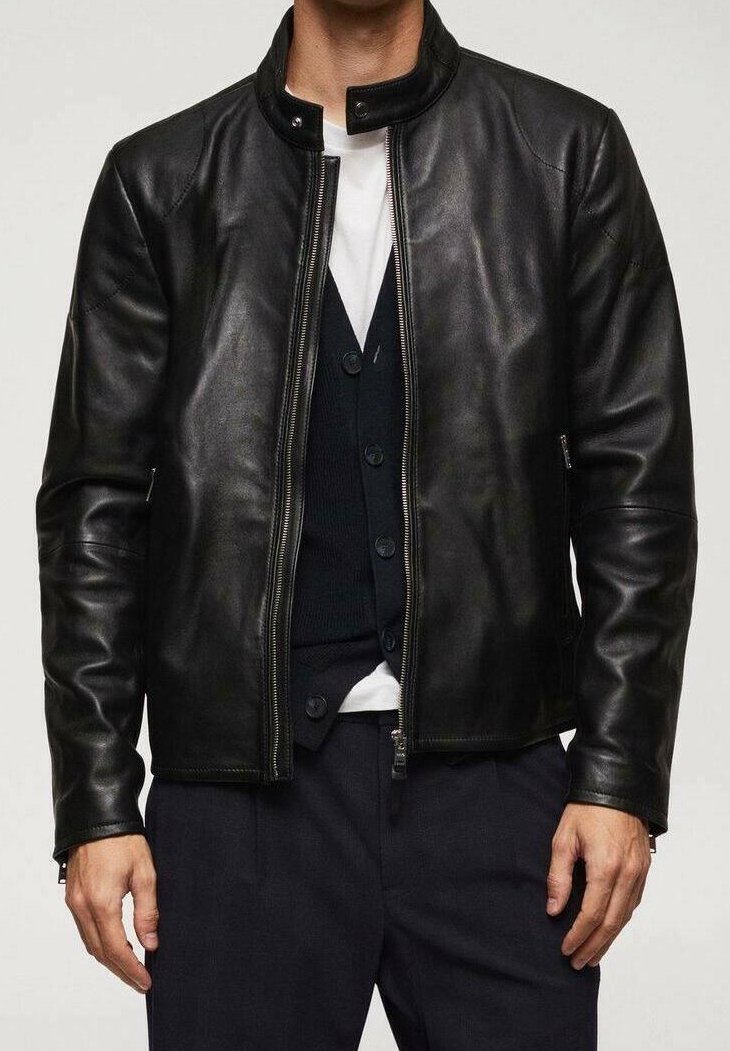 Homme portant une veste en cuir noire par-dessus un cardigan noir boutonné et un t-shirt blanc, associé à un pantalon foncé.