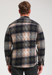 Gequilted jas in donkerblauw, beige en groene ruitpatroon. Bevat een kraag, zijslitsen en een textuurstof.
