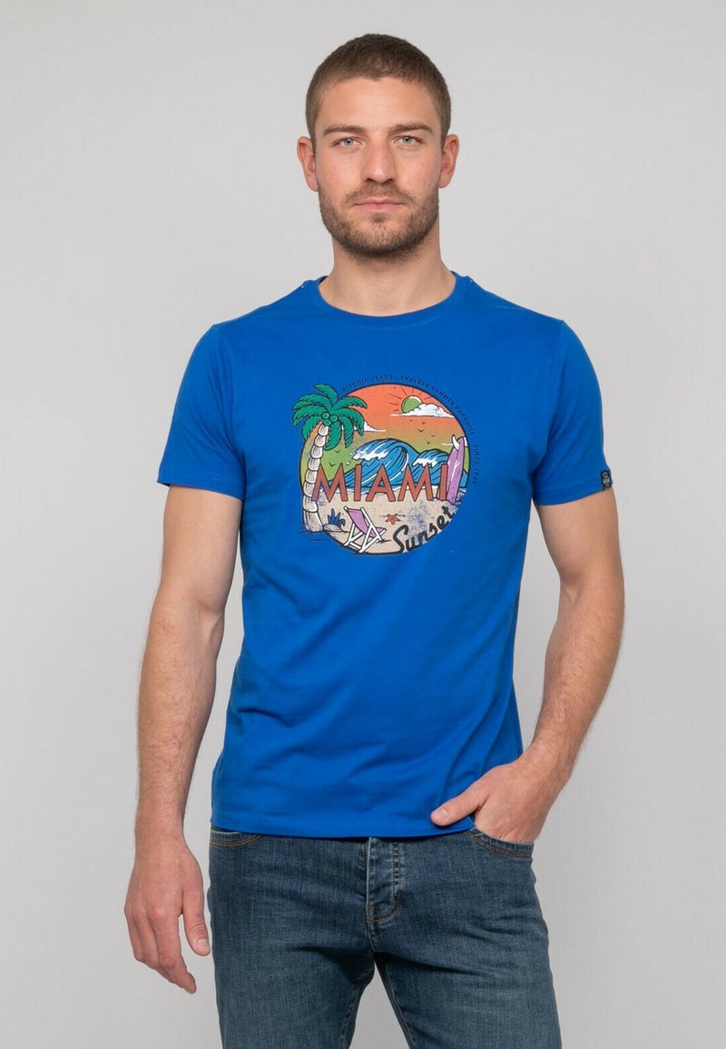 T-shirt en coton bleu avec un motif circulaire représentant des palmiers, des vagues et le texte "MIAMI Sunset" en couleurs vives et en lettres en gras.