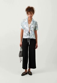 Blomstret kortermet bluse i lyseblå, med rynket front og knytedetalj. Kombinert med svarte vide bukser og svarte sandaler.