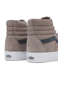 Un paio di sneaker alte Vans in suede grigio con suole bianche e strisce nere laterali, viste da dietro su uno sfondo bianco.