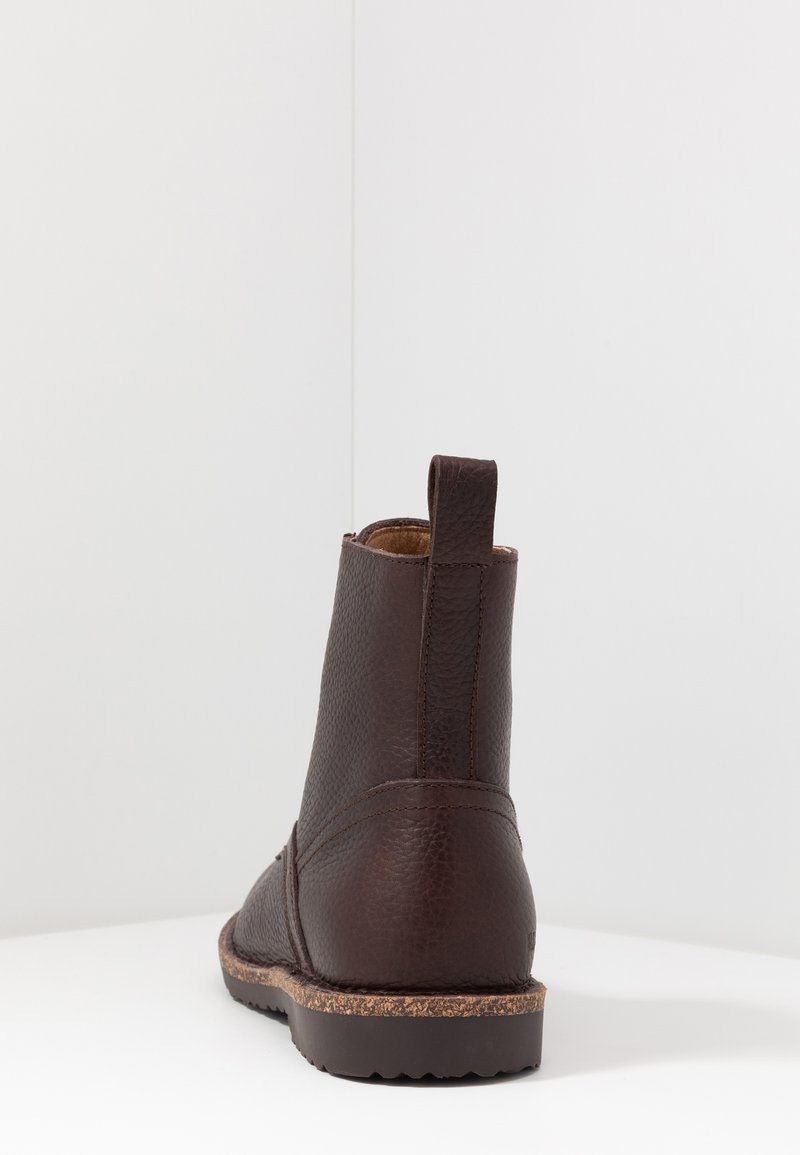 Braune Lederstiefelette mit strukturiertem Finish, geschwungenem Knöchel und flacher Sohle, die entlang der Kante einen Korkakzent aufweist. Mit einem Zuglasche an der Rückseite.