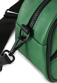 Sac bandoulière en cuir synthétique vert avec fermeture éclair, quincaillerie noire et bandoulière réglable. Présente une forme arrondie et des coutures visibles.