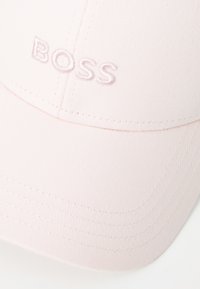 Világos rózsaszín sapka strukturált dizájnnal. Hímzett "BOSS" logó, texturált anyag és ívelt napellenző, látható varrási részletekkel.
