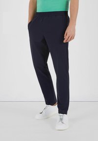 Marineblå joggebukser med elastisk talje, sidelommer og afslappet pasform, parret med hvide sneakers og en grøn skjorte.