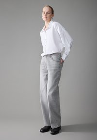 Jeans anchos grises de denim, combinados con una camisa blanca de botones de corte holgado. El conjunto incluye botas negras hasta el tobillo y pendientes de aro.