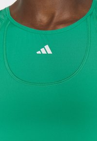 Gros plan d’une personne portant un haut de sport vert avec un logo blanc centré sous l’encolure.
