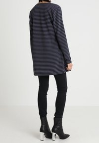 Tunique longue rayée marine, réalisée en tissu doux, présente une coupe décontractée, des poches latérales et tombe au milieu des cuisses, associée à un jean skinny noir et des bottines.