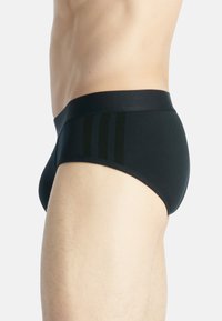Svarta kalsonger i brief-stil gjorda av smidigt tyg, med ett brett midjeband och tre vertikala ränder i en mörkare nyans på sidan.