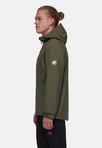 Oliwkowa wodoodporna kurtka z kapturem, z zamkiem z przodu, boczną kieszenią i naszywką z logo na lewym rękawie; miękka tekstura i opływowy design.