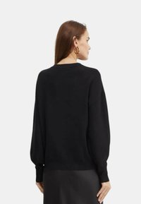 Maglione nero a maglia con spalle cadute, polsini a costine e scollo rotondo. Texture morbida; si ferma in vita con una vestibilità rilassata.