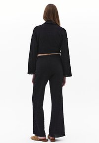 Černý texturovaný dvoudílný outfit se zkrácenou bundou s dlouhými rukávy a širokými kalhotami. Materiál má mačkaný vzor.