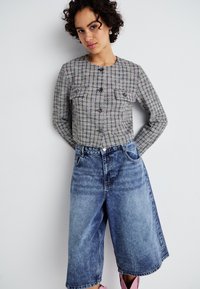 Veste à carreaux gris avec deux poches avant, fermeture à boutons et manches longues, associée à un short bermuda en denim bleu décontracté.