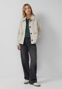 Light grey wool-blend jacket with large front pockets, black buttons, and a pointed collar, paired with dark wide-leg jeans and sneakers.
