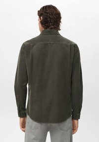 Camisa de manga larga verde olivo con cuello tipo polo, textura suave y puños abotonados. Presenta un dobladillo recto y un diseño minimalista.