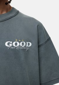 Oversized grijze sweatshirt met een ribgebreide ronde hals, met "GOOD" in het wit en "For Nothing" in cursief, met daarboven drie gouden sterren.