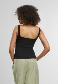 Top negro sin mangas ajustado con tirantes finos, textura suave y escote cuadrado, combinado con pantalones de cintura alta de color verde claro.