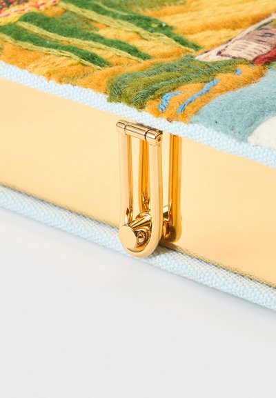 Gros plan d’un fermoir en or attaché à une housse en tissu duveteux multicolore sur un objet rectangulaire avec un bord bleu clair.