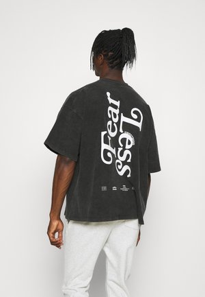 Oversized black cotton t-shirt featuring white, diagonal "Fearless" lettering on the back. Short sleeves and a crew neckline.