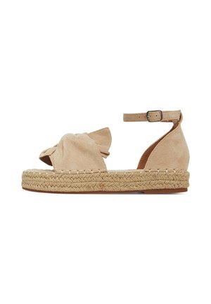 Beige suède espadrille sandaal met een knoopdetail aan de voorkant, enkelriem en een plateauzool van gevlochten touw. Kenmerkt zich door een gladde textuur en afgeronde vorm.