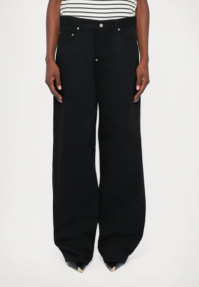 Schwarze weite Jeans mit metallischen Nieten, Fünf-Taschen-Design und einer weichen Textur, kombiniert mit einem gestreiften Oberteil für den Kontrast.
