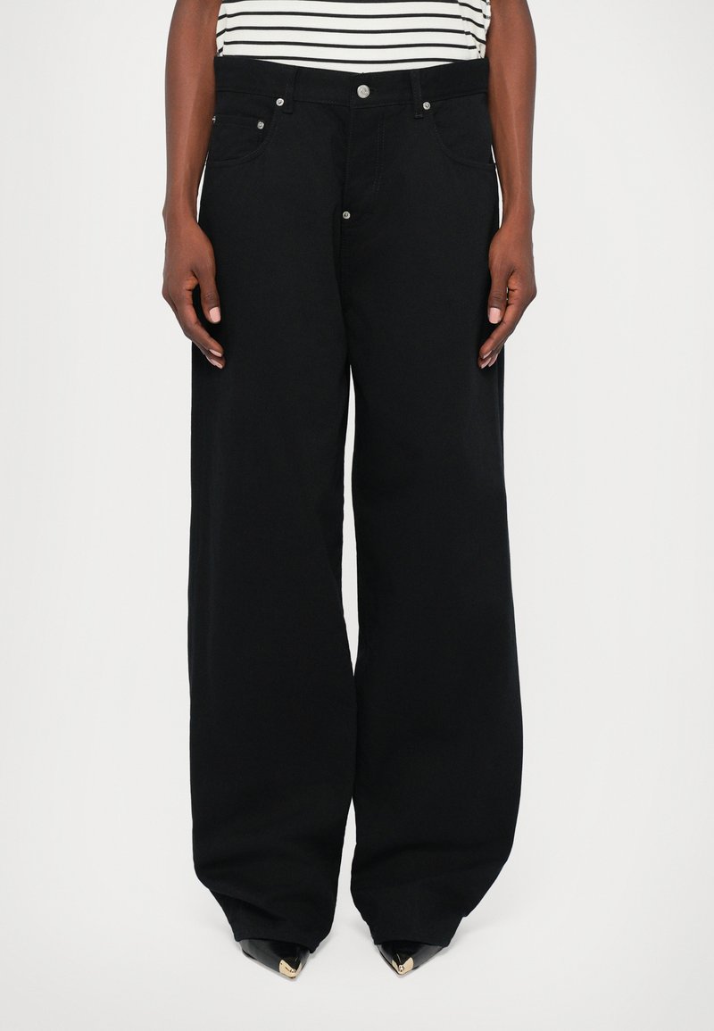 Schwarze weite Jeans mit metallischen Nieten, Fünf-Taschen-Design und einer weichen Textur, kombiniert mit einem gestreiften Oberteil für den Kontrast.