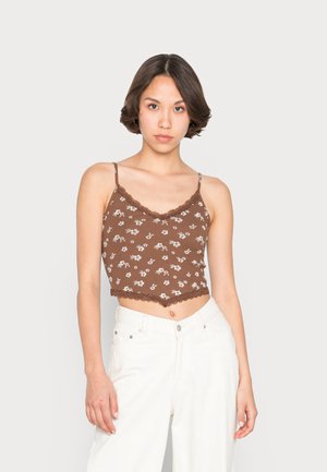 Top cropped com padrão floral castanho e acabamento em renda, apresentando alças finas de espaguete e textura ribada. Combinado com calças brancas de perna larga.