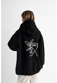 Felpa nera con un grande disegno bianco di un volto e una foglia sul retro. Presenta un design ampio e un cappuccio grande.