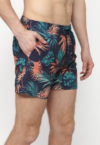Șorturi de înot de culoare albastru marin cu un model de frunze tropicale în nuanțe de verde și corai. Au talie elastică și buzunare laterale.