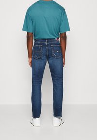 Ciemnoniebieskie dżinsy o slim fit, z dwiema tylnymi kieszeniami i kontrastowym przeszyciem. Połączone z turkusową koszulką z krótkim rękawem.