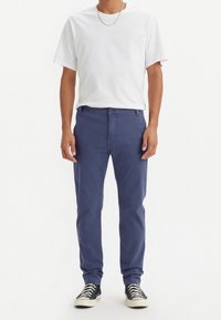 Tmavě modré bavlněné chino kalhoty s přímým střihem, vybavené zapínáním na knoflíky, poutky na pásek a předními kapsami, doplněné bílým tričkem s kulatým výstřihem.