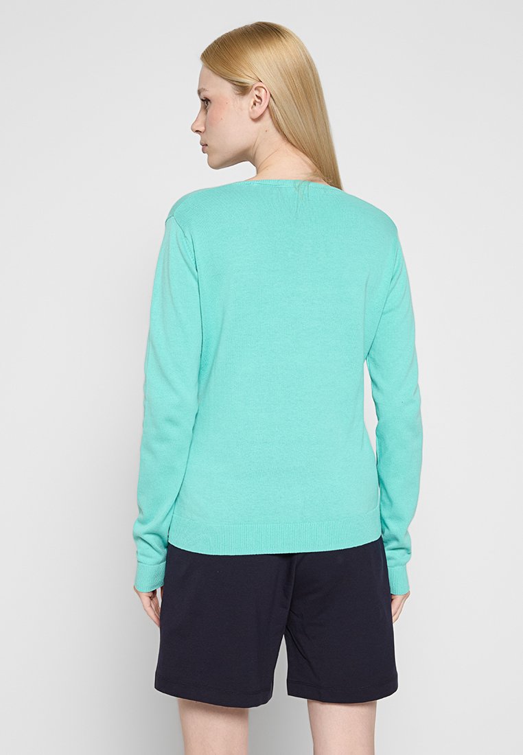 Hellblauer Pulli mit rundem Ausschnitt und geripptem Saum. Der Stoff wirkt glatt und wird durch ein minimalistisches Design ergänzt. Kombiniert mit navyblauen Shorts.