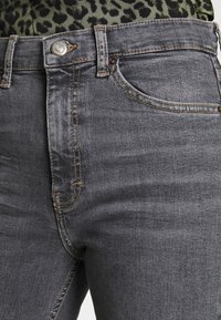 Vaqueros de mezclilla gris de corte slim, con un botón plateado, detalles de costura y una sutil textura deslavada. Bolsillo frontal visible.