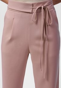 Blush roze broek met een hoge tailleband en voorplooien. Heeft een stoffen strik in de taille, gemaakt van een gladde, lichte stof.
