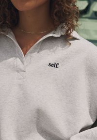 Hall toonikaga hall pusa, rinnaosas musta tikandiga tekstiga "self." Pehme kangast tekstuur ja mugav lõige.