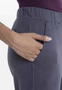 Joggers gris avec une texture douce, dotés d'une taille élastique et de poches latérales. Gros plan d'une main reposant dans la poche.