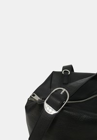 Borsa di pelle nera con finitura testurizzata, dotata di una fibbia e di una cerniera in argento. Il design include una tracolla piatta e una forma strutturata.