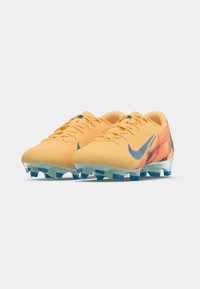 Kollased jalgpalliketsid tekstureeritud pinnaga, sinise Nike logosid ja gradientehnikat sisaldav disain, selge tald, millel on vormitud nupud haardevõime tagamiseks.