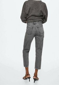 Jeans de tiro alto a rayas blancas y negras con corte recto, que presentan dos bolsillos traseros y un dobladillo sin terminar, combinados con tacones negros con tiras.