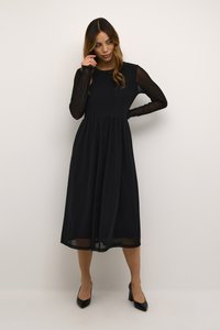 Robe midi noire avec un haut ajusté, des manches longues transparentes et une jupe fluide. Accompagnée de chaussures à talons hauts noires.