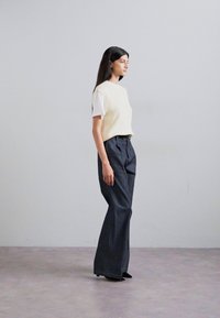 Un haut sans manches à rayures jaune clair sur une chemise blanche, associé à un pantalon sombre taille haute. L'ensemble est complété par des chaussures noires.