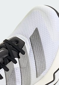 Scarpa sportiva bianca con tomaia in rete traspirante, lacci neri e dettagli texture in grigio. Presenta una suola ammortizzata e un design elegante.