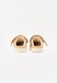 Ballerines beiges à enfiler avec un intérieur doux et moelleux, semelle plate et une sangle ajustable à l'arrière ; design minimaliste avec des détails de couture subtils.