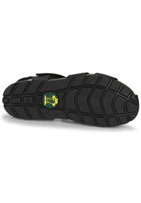 Suela de sandalia negra con patrón de relieve de goma texturizada. Incluye un detalle del logo en verde y un borde elevado y robusto para un mejor agarre.